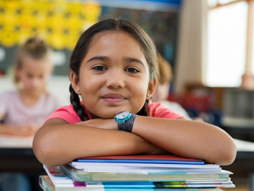 Young girl in school resting on a stack of books